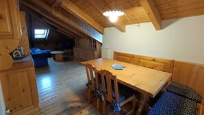 Een houten eethoek met een tafel, stoelen en een bank, en een plafondlamp.