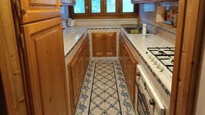 Een smalle keuken met houten kastjes, een betegelde vloer en een gasfornuis.