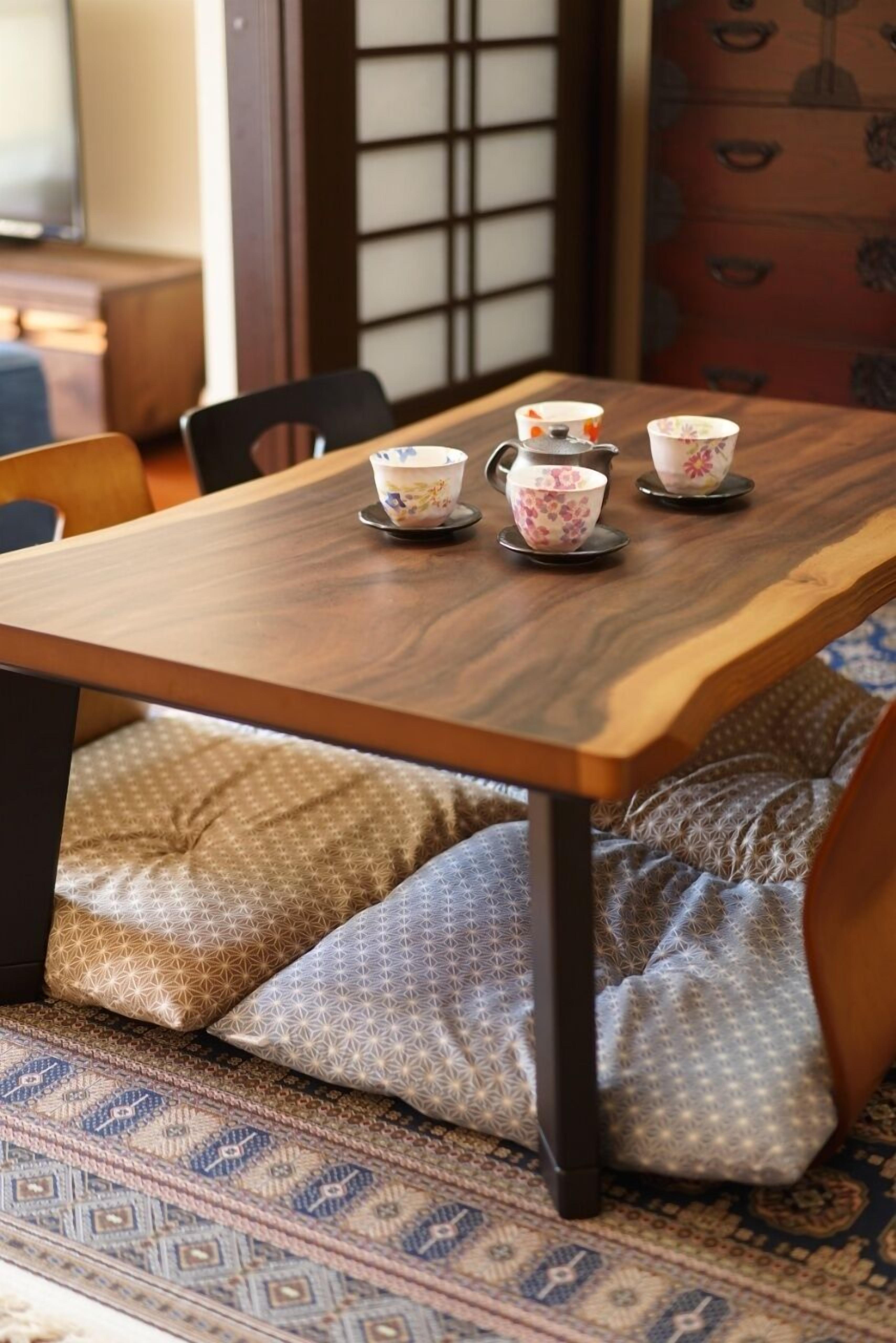 A wooden table with floral-patterned cups and saucers, a patterned cushion, and a traditional Japanese sliding door in the background.