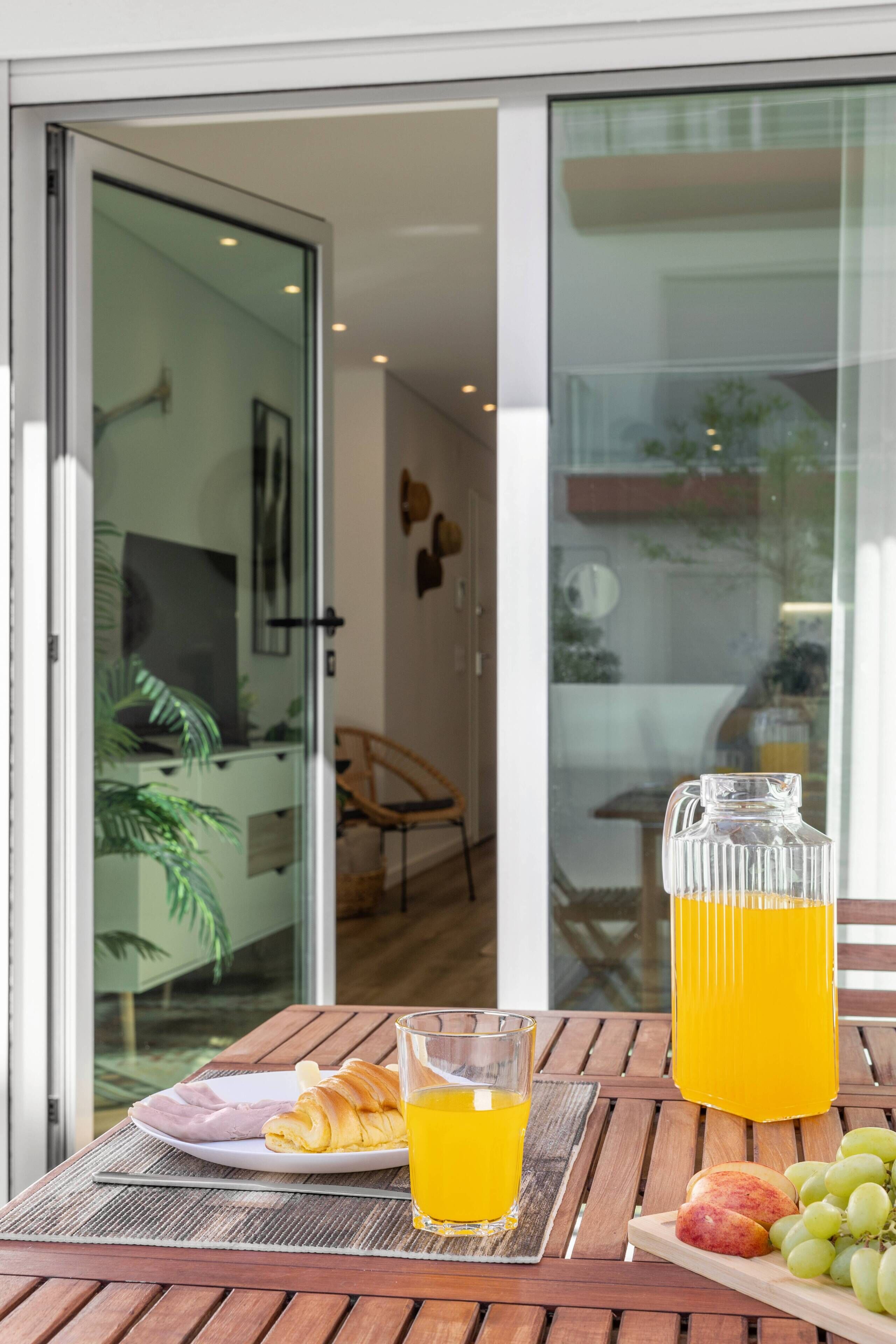 A breakfast table with croissants, a glass of orange juice, and a pitcher of orange juice.