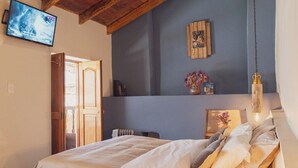 A cozy bedroom with a wooden ceiling, a bed with white linens, a wooden nightstand, and a TV mounted on the wall. - Dona Catta Boutique Loft—Just 10 minutes from the station! (Ollantaytambo)
