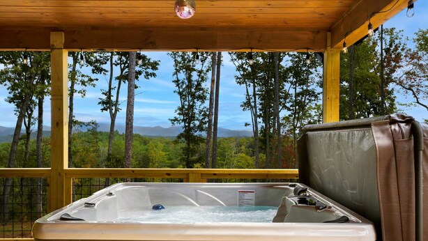 Een hottub op een houten terras met uitzicht op bomen en bergen.