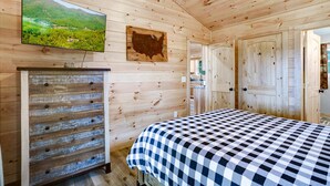 Een houten kamer met een bed, een dressoir, een televisie en een deur.