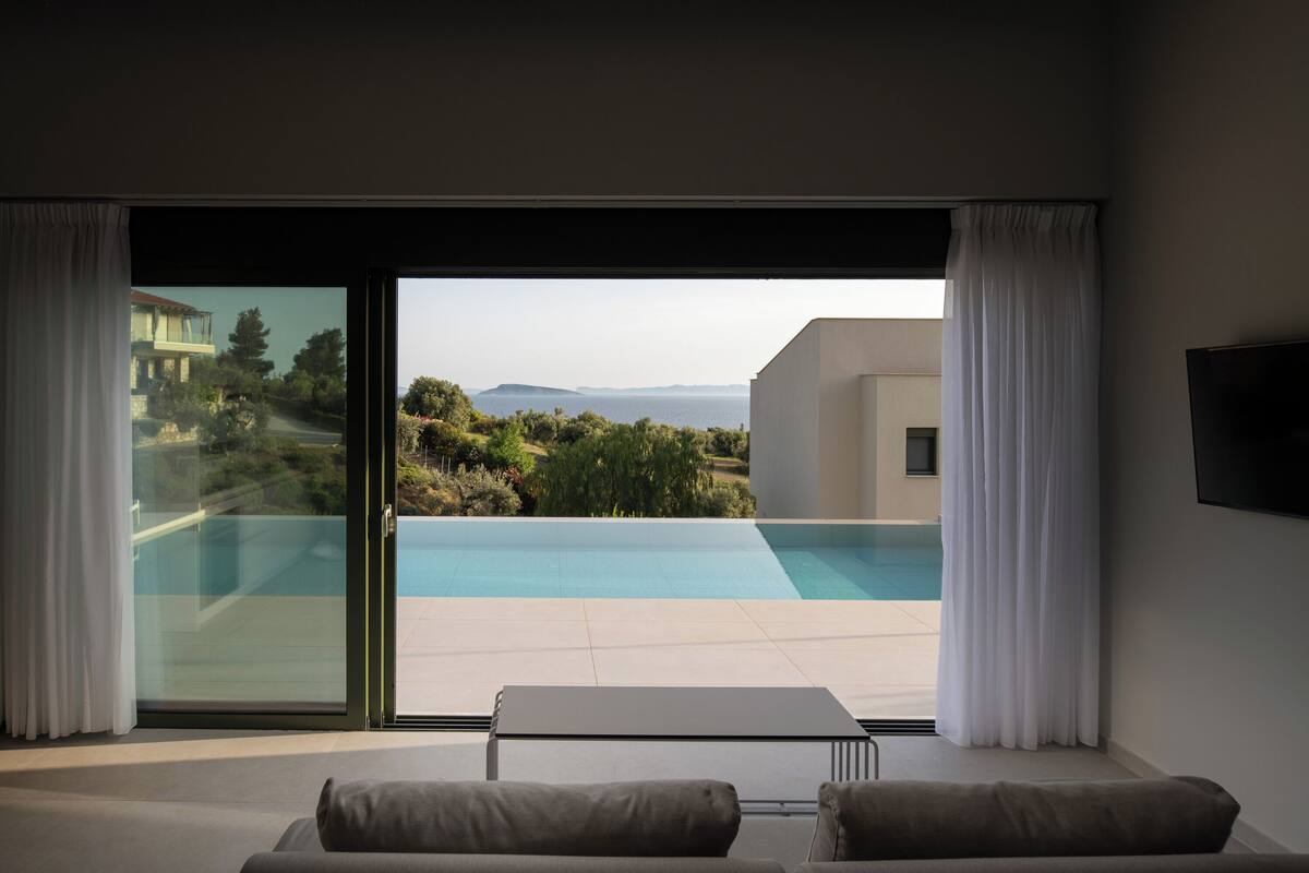 A modern room with a large sliding glass door leading to a pool, a sofa, and a flat-screen TV.