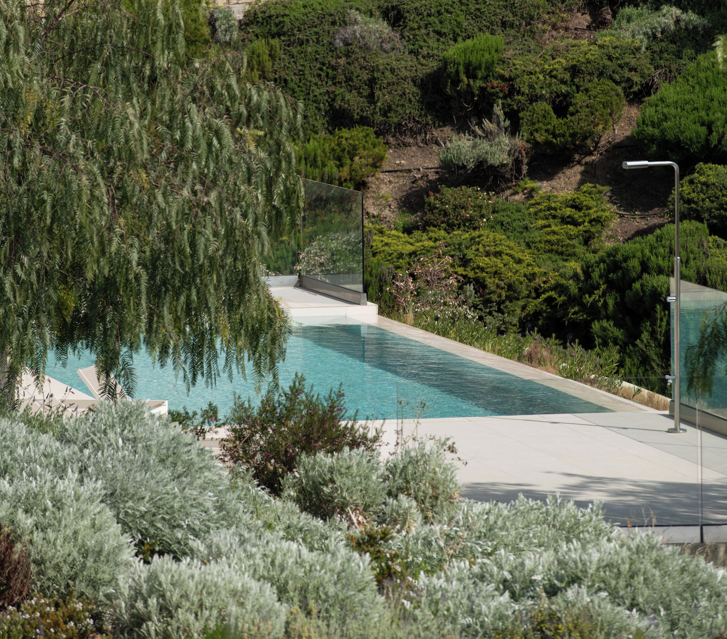 Une piscine moderne à l’eau d’un bleu cristallin, entourée d’une végétation luxuriante et adossée à une colline.