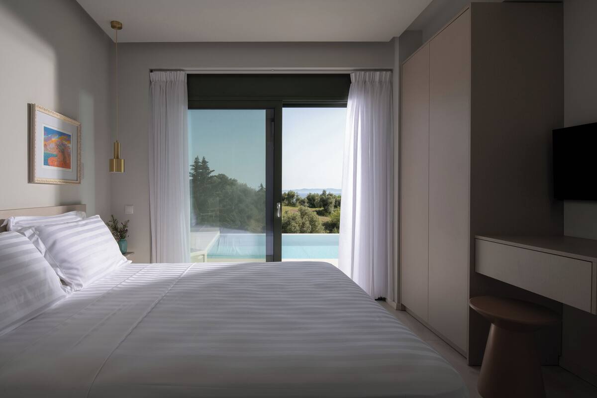 A bedroom with a large bed, a desk, and a view of a pool and greenery.
