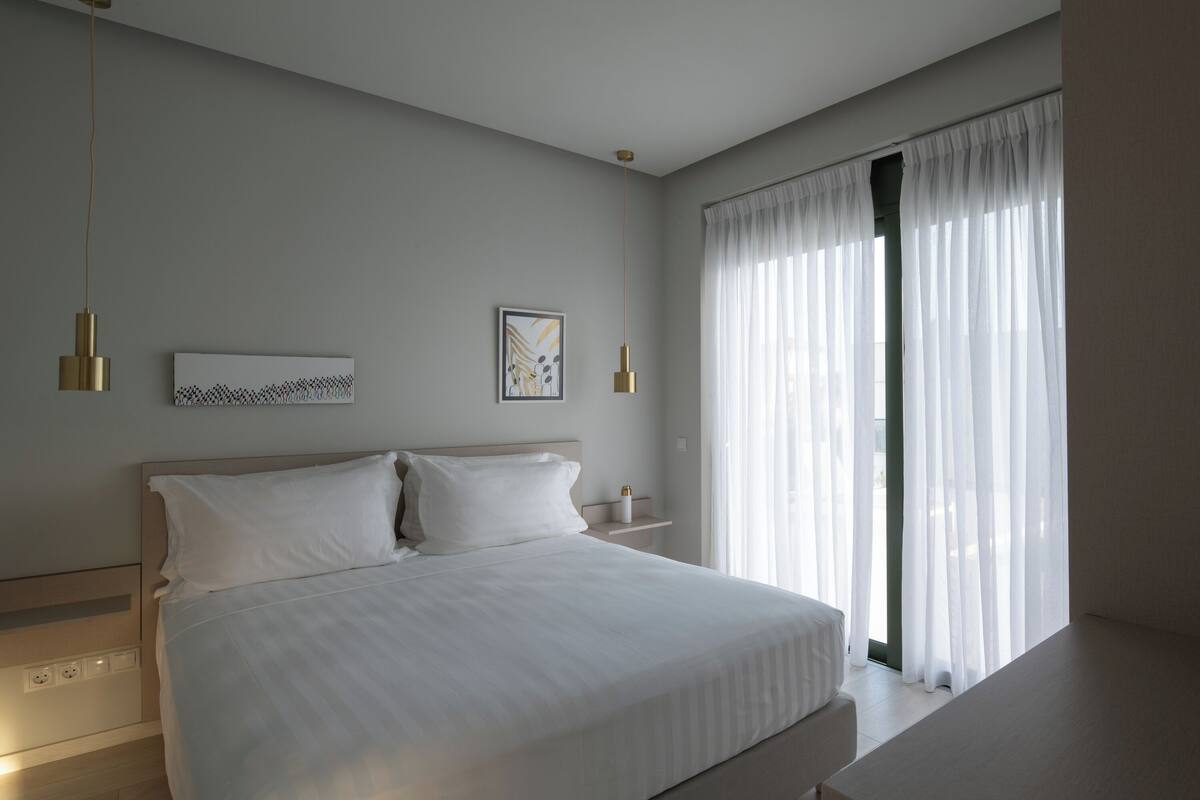 A modern bedroom with a large bed, bedside tables, and a window with sheer curtains.