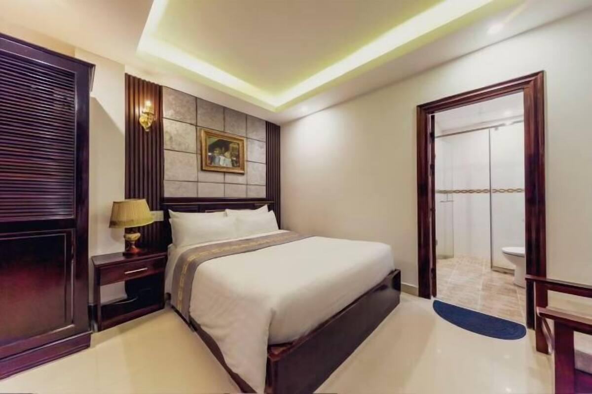 A hotel room with a bed, nightstand, wall-mounted lamp, and a painting.