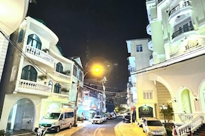 Vista nocturna de una calle con edificios, automóviles estacionados y un farol.