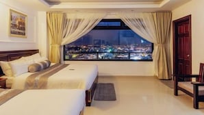 Ein Hotelzimmer mit einem großen Bett, Blick auf eine Stadtlandschaft und einem fenster mit Vorhängen.