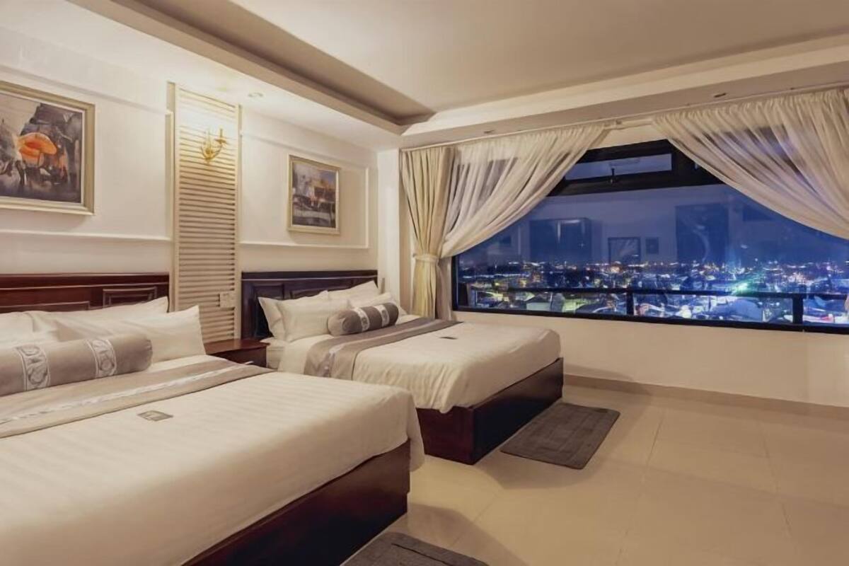 A hotel room with two beds, a city view, and a large window with curtains.