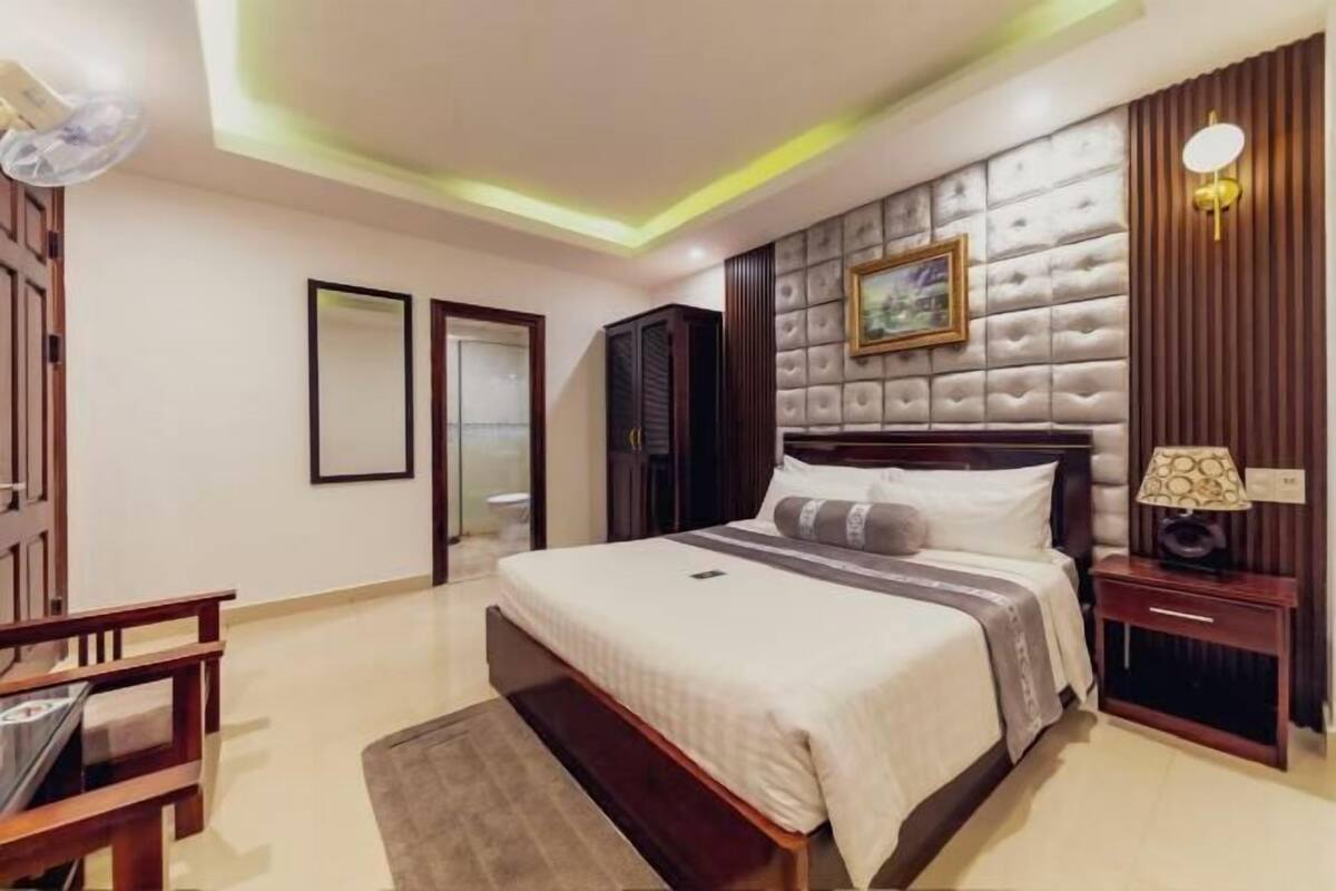A hotel room with a large bed, a bedside table, a nightstand, a wall-mounted TV, and a ceiling fan.