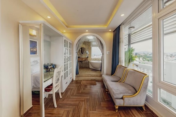 A corridor with a sofa, a dining area, and a view through large windows.