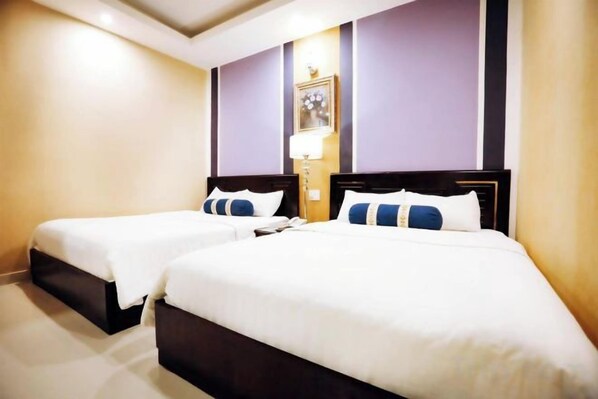 A hotel room with two beds, a nightstand, and a wall-mounted lamp.