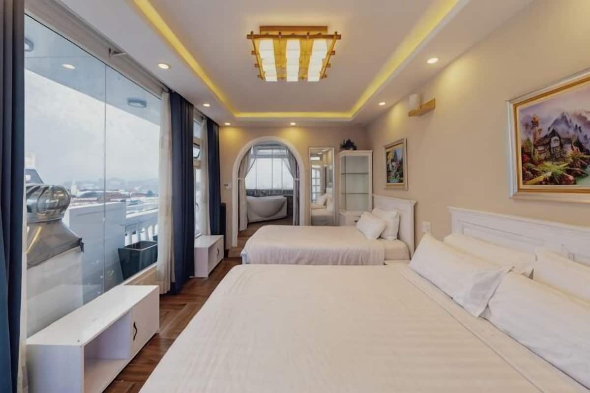 A hotel room with two beds, a large window, a bathtub, and a view of the city.