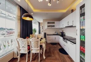 A modern kitchen with white cabinets, a dining area with white chairs, and a view through large windows.