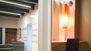 A modern office space with a wooden floor, a desk with a chair, and a wall-mounted lamp. - Gîtes de France® - Paty (CAJARC)