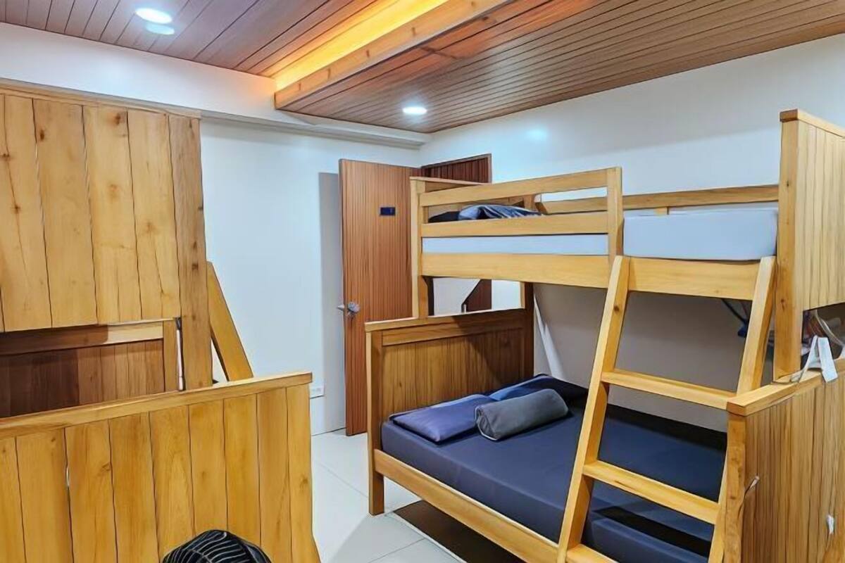 A bunk bed with a wooden frame and a mattress, a wooden wardrobe, and a door to a bathroom.