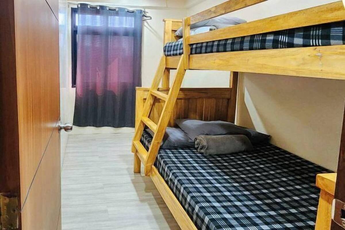 A bunk bed room with a wooden ladder, checkered bedding, and a curtain.