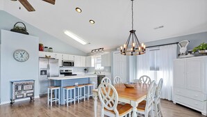 A spacious kitchen with a wooden dining table and white chairs, a built-in oven, and a hanging light fixture. - Practically Perfect on West Beach - Just steps away from the Atlantic Ocean (Oak Island)