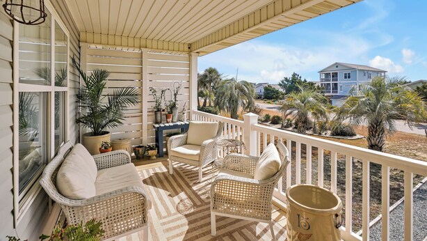 A covered porch with wicker furniture, potted plants, and a view of a residential area. - Practically Perfect on West Beach - Just steps away from the Atlantic Ocean (Oak Island)
