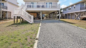 A two-story house with a covered porch and a staircase leading to a balcony. - Practically Perfect on West Beach - Just steps away from the Atlantic Ocean (Oak Island)