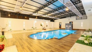 An indoor swimming pool with a wooden floor, surrounded by potted plants and a stone wall.
