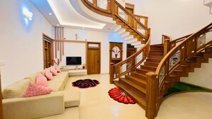 A modern living room with a curved staircase, a sofa set, and a flat-screen TV.