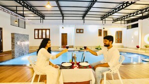 Una pareja cenando junto a una piscina, con una mesa dispuesta para dos, una cascada decorativa y un diseño interior moderno.