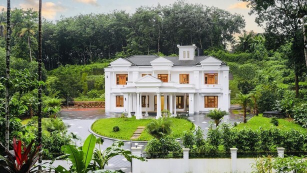 A large, white colonial-style house with a symmetrical facade, multiple windows, and a central entrance.