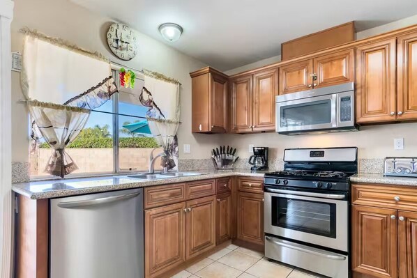 A kitchen with wooden cabinets, stainless steel appliances, and a window with decorative curtains.