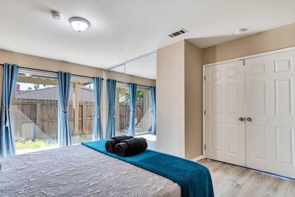 Un dormitorio con una cama grande, una ventana con cortinas, una puerta corredera y vistas al patio trasero.
