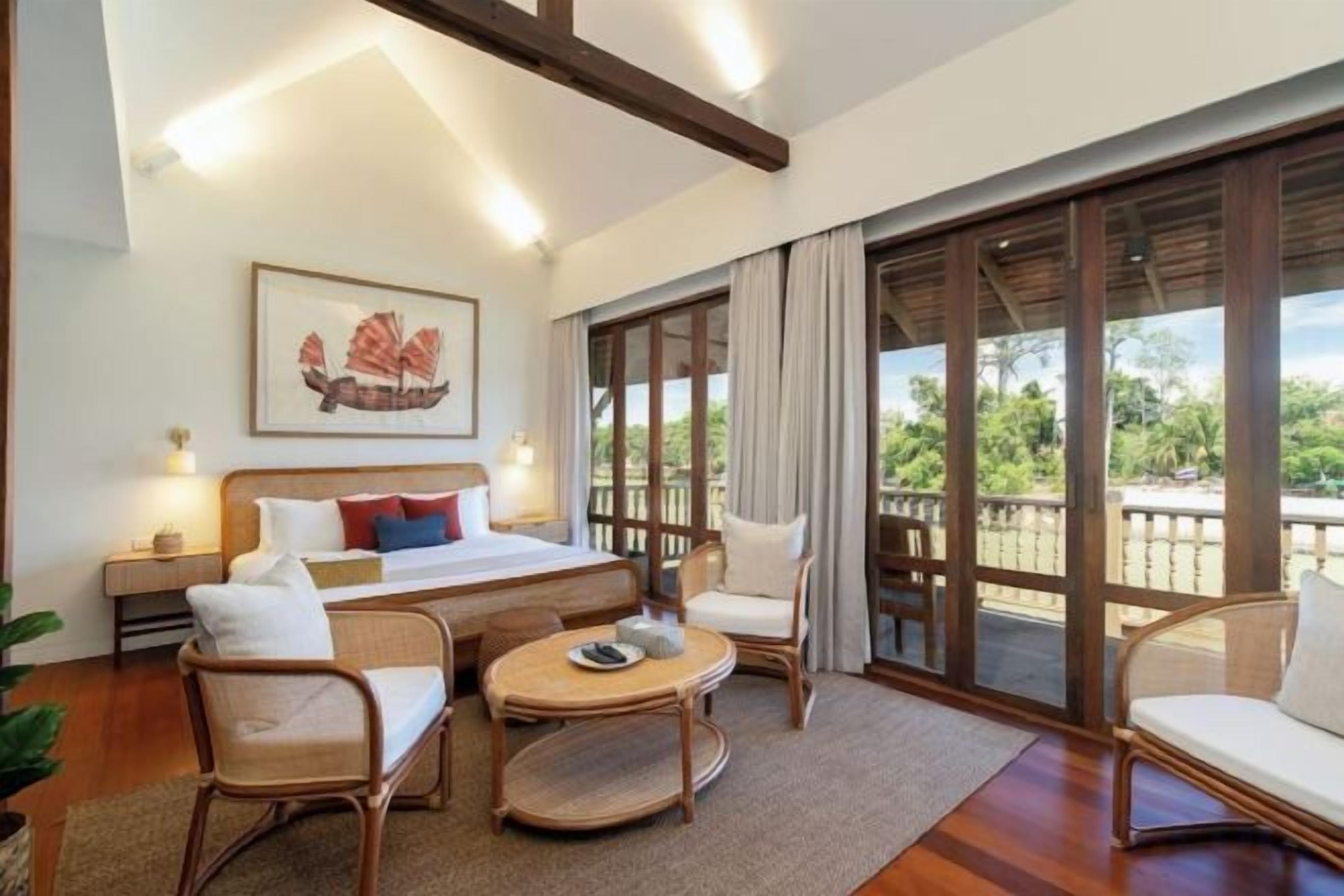 Habitación de hotel con cama, dos sillas, una mesita y un ventanal con vistas a zonas verdes.