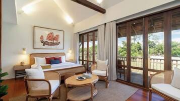 Habitación de hotel con cama, dos sillas, una mesita y un ventanal con vistas a zonas verdes.