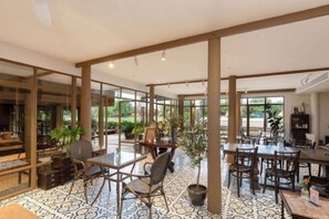 A spacious indoor area with multiple tables and chairs, large windows, and a patterned floor. - Syama Residence and Café (Phra Nakhon Si Ayutthaya)