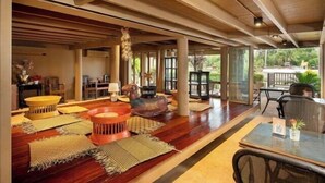 Um quarto espaçoso com piso de madeira, divisória de vidro e área de refeições com cadeiras e mesas.