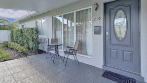 Il s’agit d’une propriété résidentielle avec une porte grise portant le numéro 210, un patio couvert avec une table et des chaises, et un petit jardin.