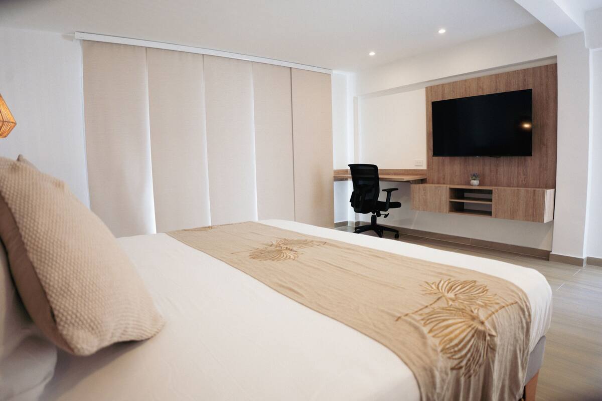 A modern hotel room with a large bed, a desk, and a TV mounted on the wall.