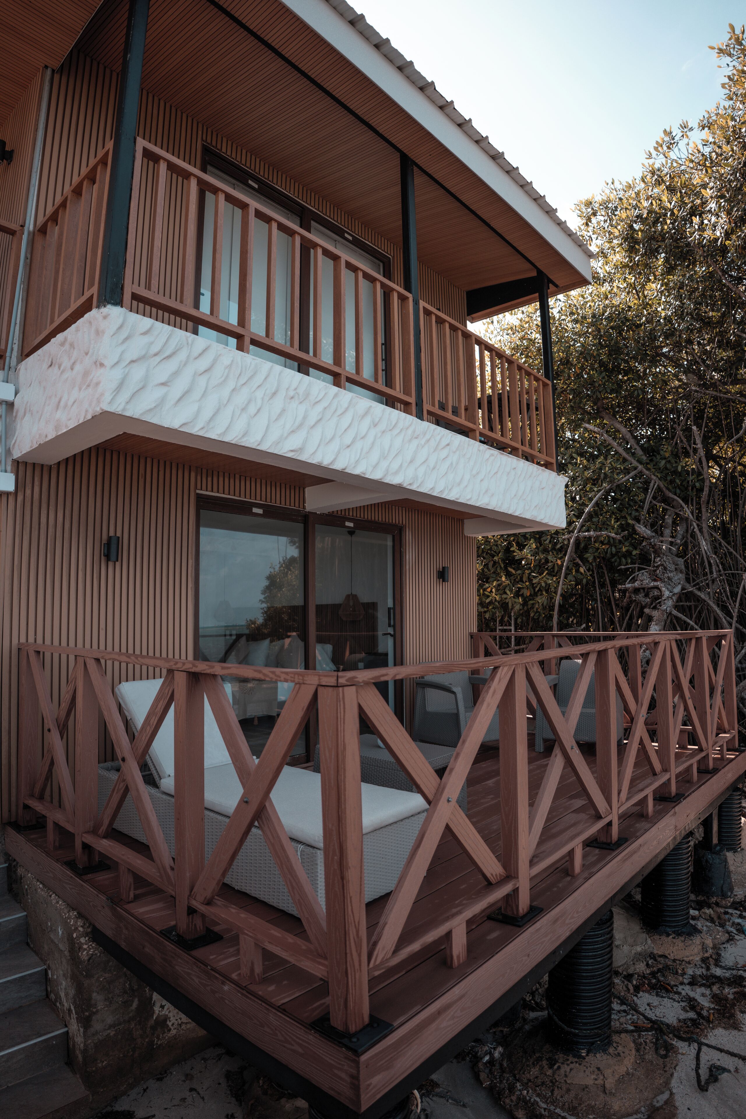 Un bâtiment en bois à deux étages, doté d’un balcon et d’un espace extérieur aménagé pour s’asseoir.