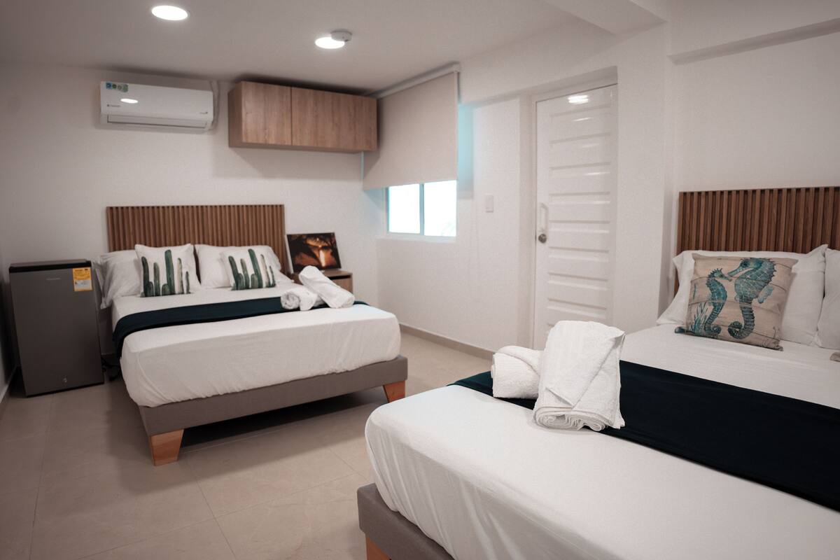 A hotel room with two beds, a wardrobe, an air conditioning unit, and a small desk.