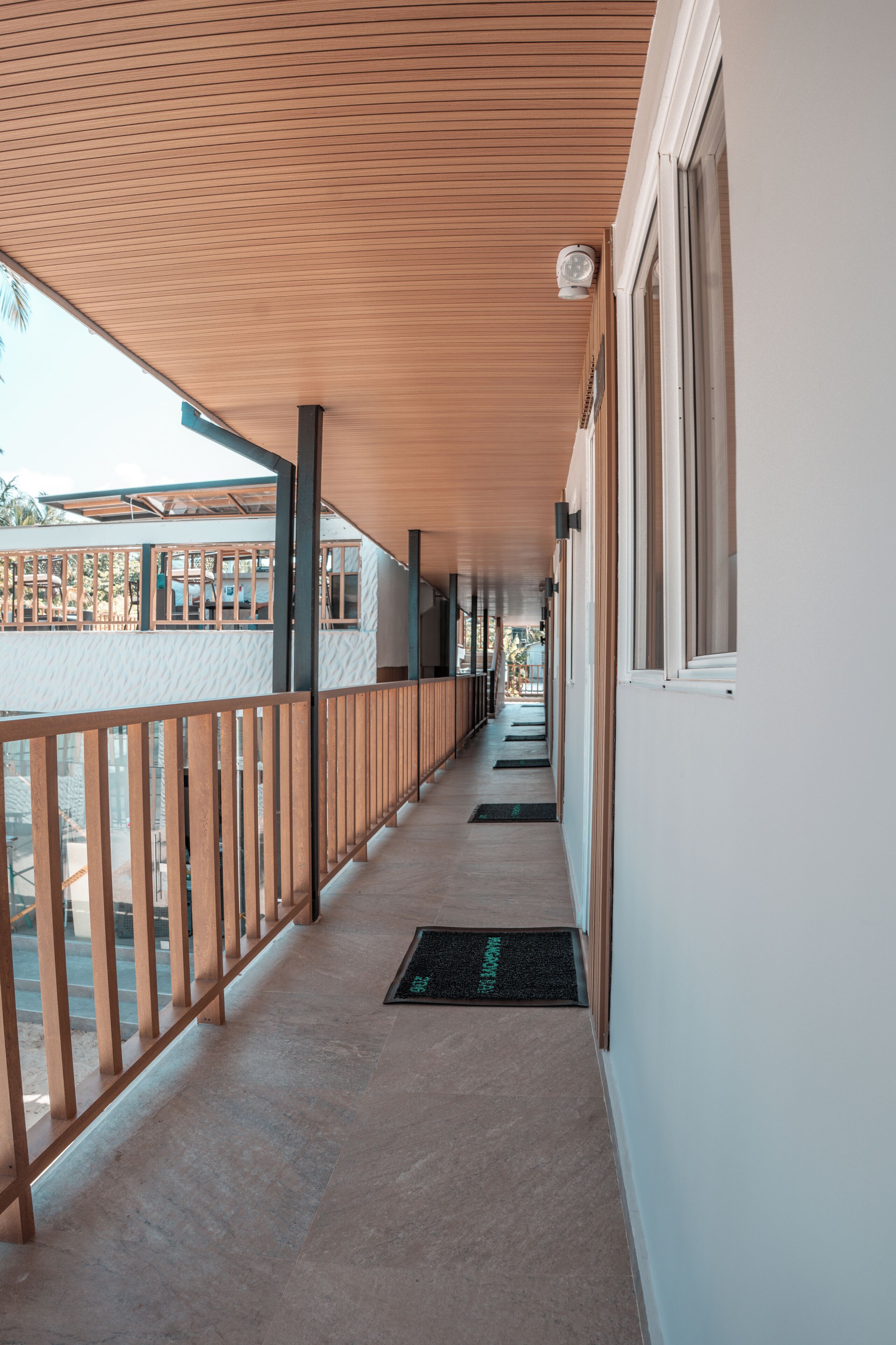 Un pasillo con barandas de madera, piso de baldosas y vistas al exterior.