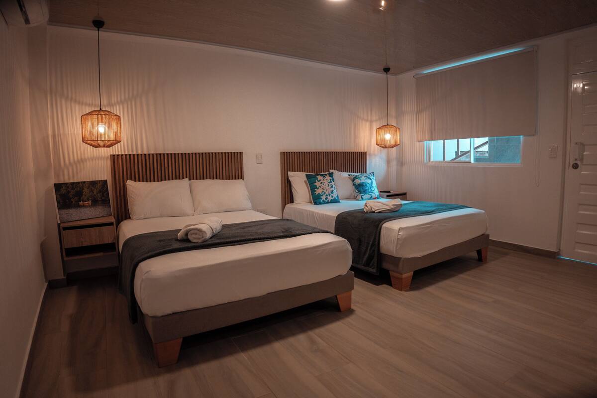 A hotel room with two beds, wooden flooring, and pendant lighting.