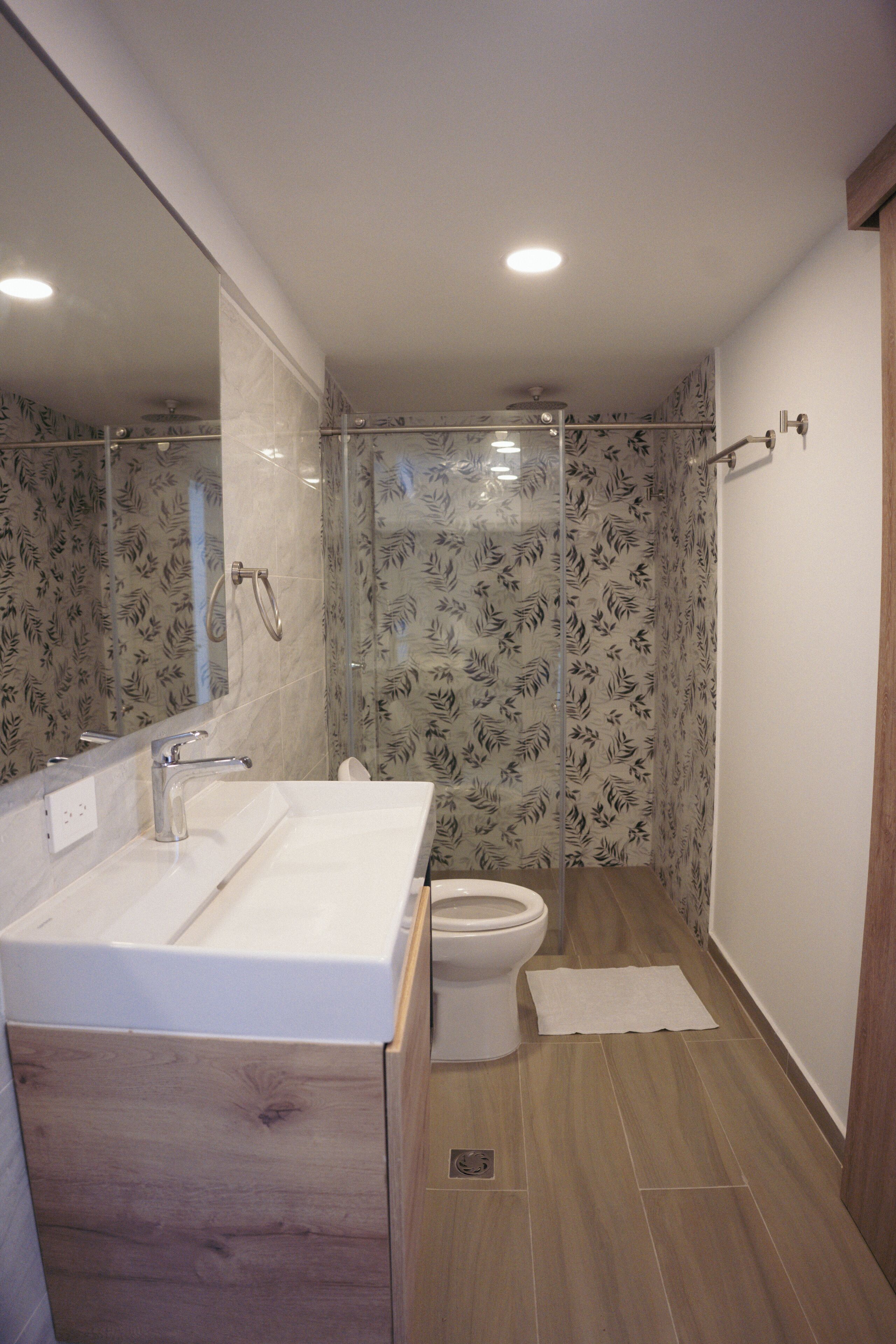Een moderne badkamer met een houten wastafelmeubel, een douchecabine van glas en een toilet.