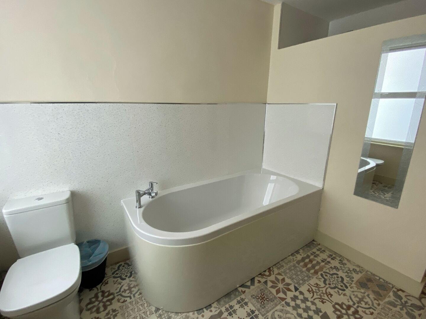 A bathroom with a bathtub, toilet, and patterned floor tiles.