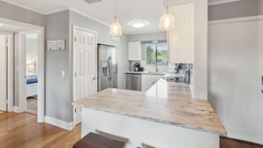 Una cocina moderna con armarios blancos, encimera de mármol e iluminación colgante.