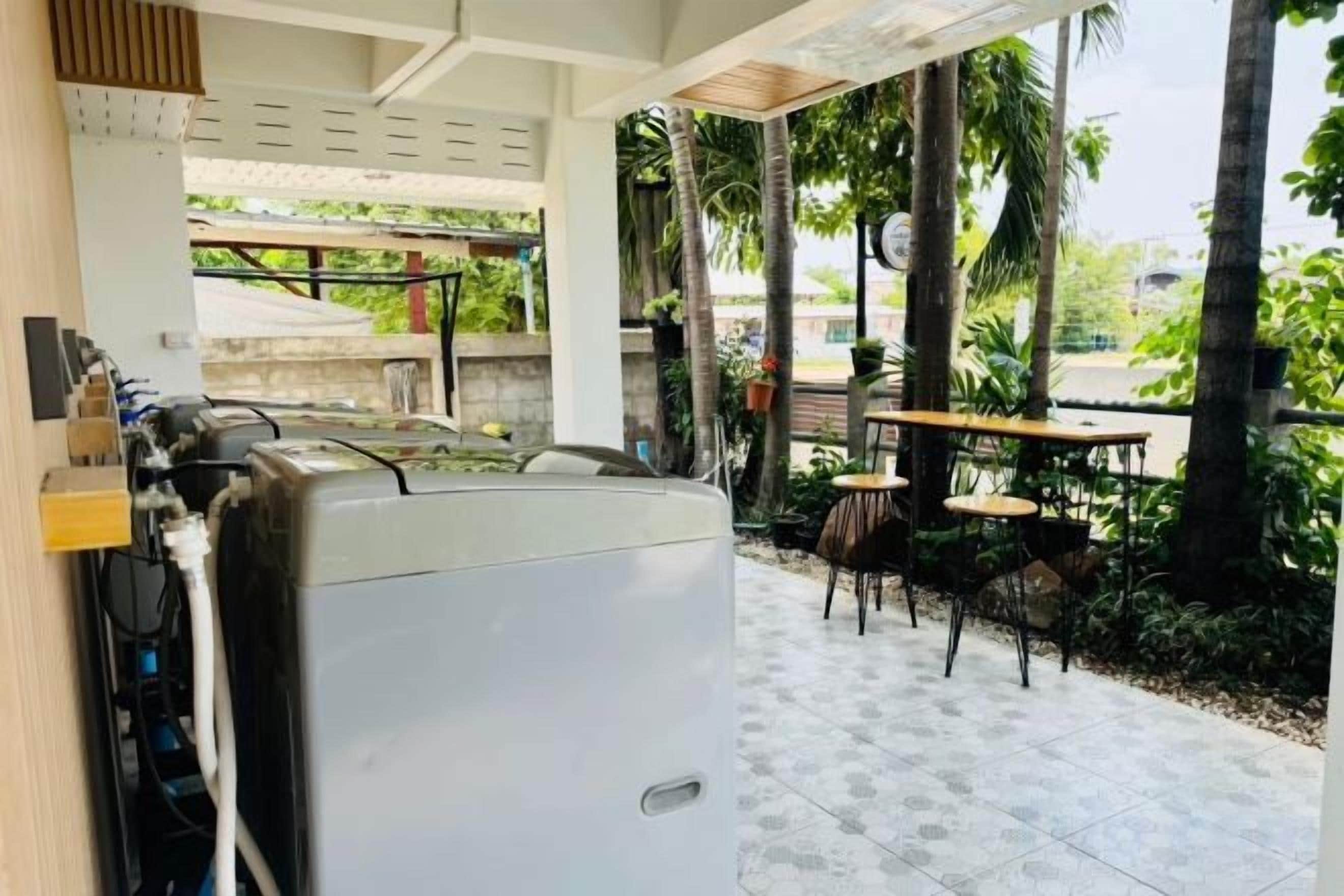 Un espacio exterior techado con mesas y sillas, un refrigerador blanco y vistas a la vegetación.