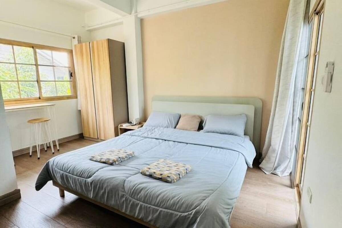 A bedroom with a bed, a window, a wardrobe, and a stool.