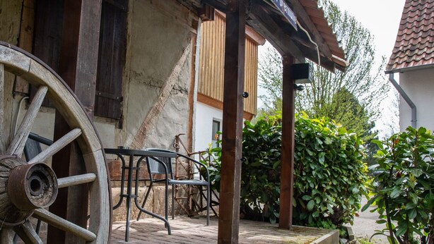 Un espacio al aire libre rústico con una gran rueda de madera, una mesa de metal y una estructura de madera con techo.