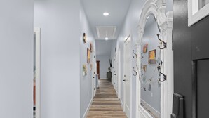 Un pasillo con piso de madera, paredes blancas y una puerta con arco decorativo.
