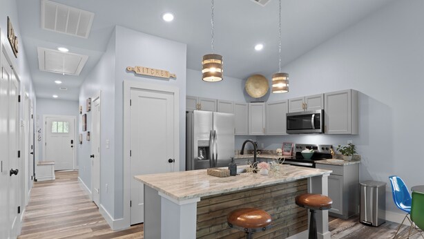 Una cocina moderna con una isla central, taburetes de bar, electrodomésticos de acero inoxidable e iluminación colgante.